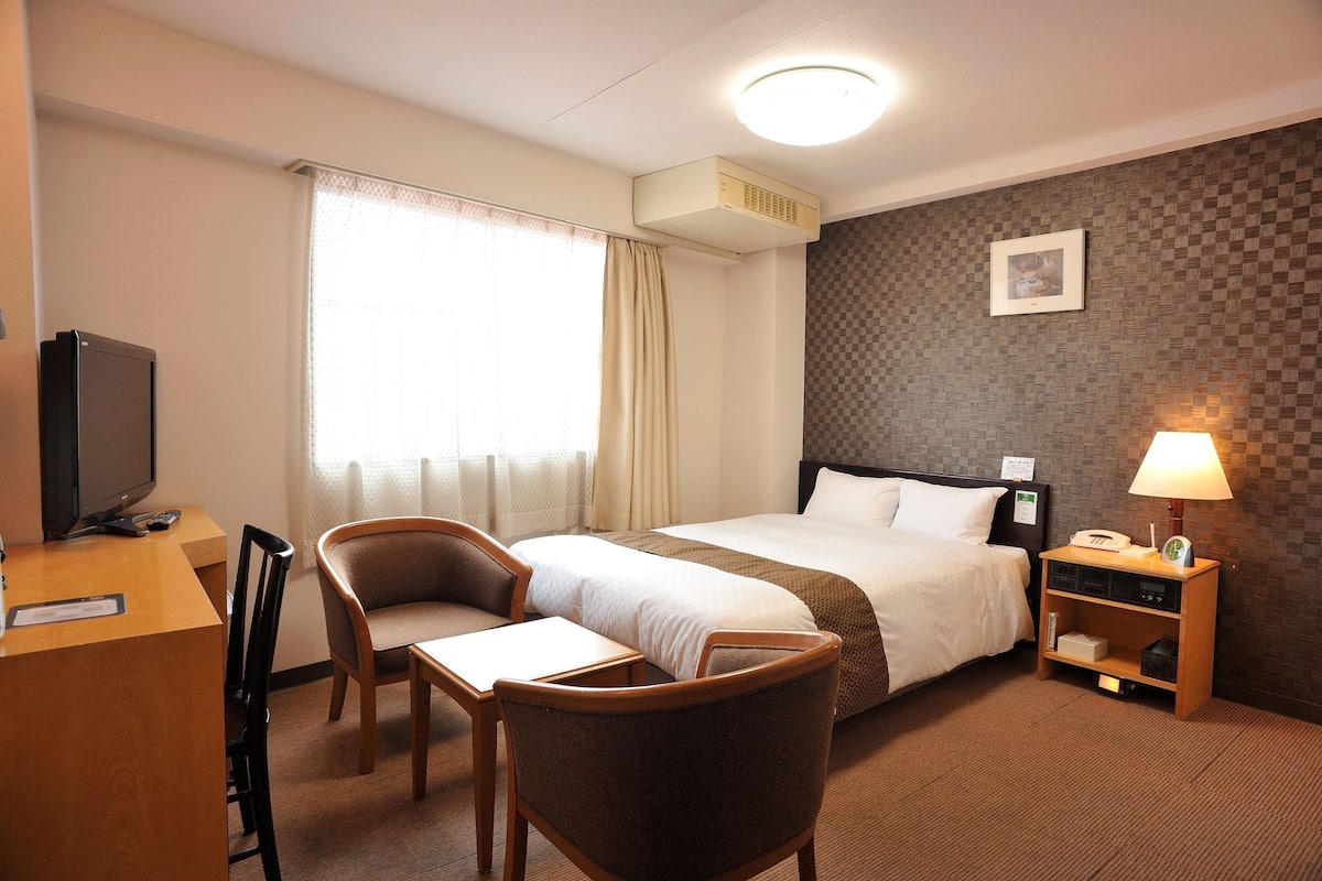 Ein Hotelzimmer mit einem Bett, einem Schreibtisch mit Stuhl, einem Fernseher und einer Lampe.
