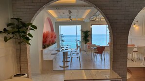 A modern interior with a view of the sea through an arched doorway. There are tables and chairs arranged for dining or sitting. - Mr. Slow (Sokcho)