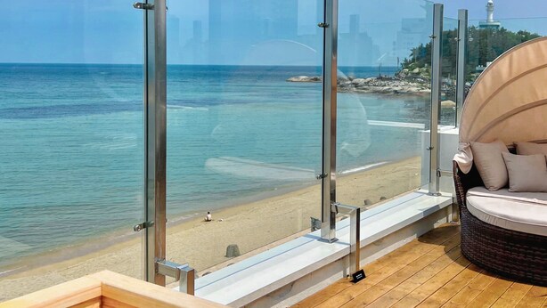 A wooden deck with a glass balustrade overlooking a beach. - Mr. Slow (Sokcho)