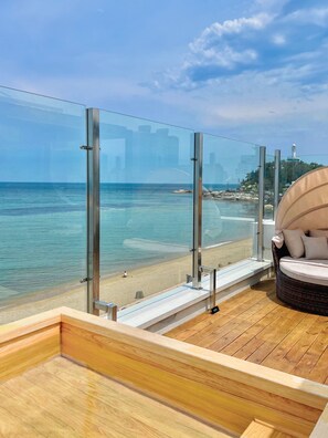 Una terraza de madera con barandilla de vidrio con vista a la playa.