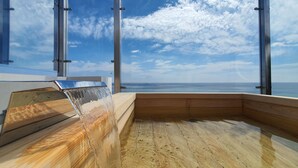 A wooden hot tub with a waterfall feature, large windows, and a view of the sea. - Mr. Slow (Sokcho)