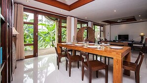 A spacious dining area with a large wooden table, multiple chairs, and a ceiling fan. - NB Villa Sienna (Koh Samui)