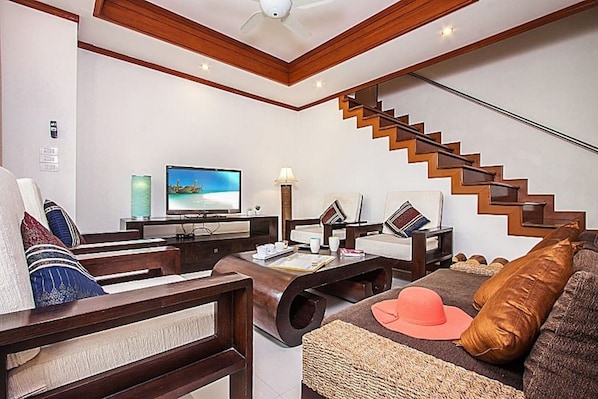 A modern living room with a wooden staircase, a flat-screen TV, and comfortable seating.
