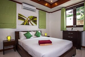 A hotel room with a large bed, green curtains, a bedside table with a lamp, and a wall-mounted air conditioner.