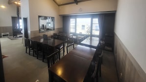 A spacious dining area with high ceilings and exposed beams, a large window with curtains, and a view of the street outside. - Hakuba Powder Lodge (Hakuba)