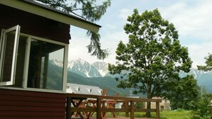 A wooden deck with chairs, a mountain view, and a building with large windows. - Hakuba Powder Lodge (Hakuba)