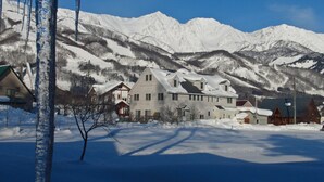 A snow-covered mountain landscape with a large house in the foreground. - Hakuba Powder Lodge (Hakuba)