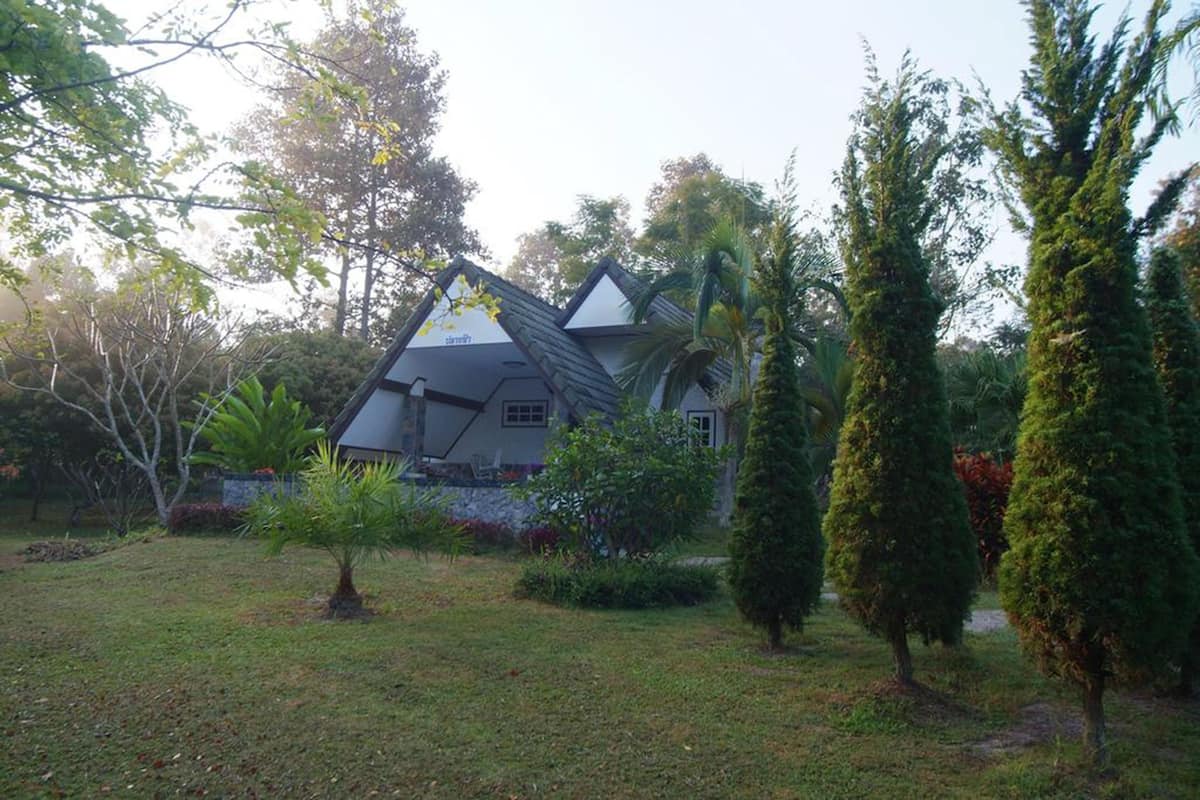 A house with a sloped roof, surrounded by a garden with various plants and trees.