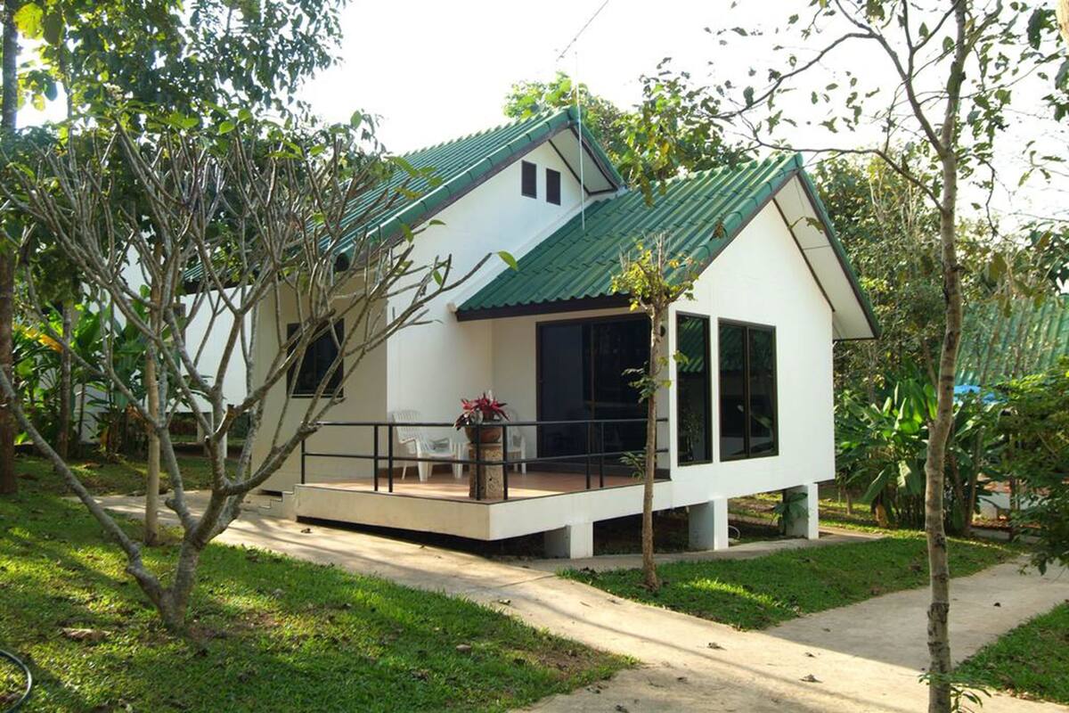 A modern house with a green roof, a balcony with chairs, and a small garden area.