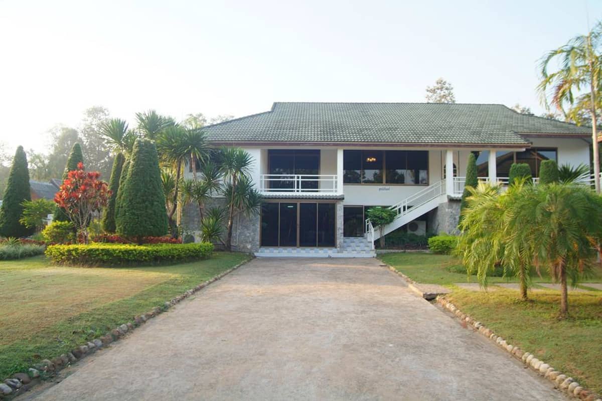 A two-story house with a covered porch, a staircase leading to the upper floor, and a well-maintained garden with palm trees and shrubs.