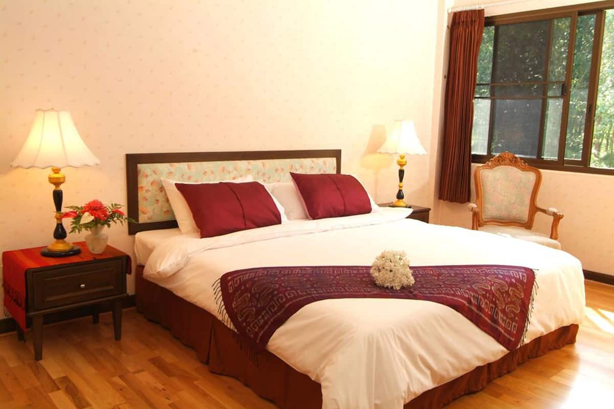 A neatly made bed with white and maroon bedding, two bedside tables with lamps, a chair, and a window with curtains.
