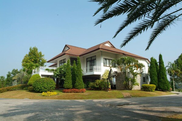 A two-story house with a balcony, surrounded by well-maintained gardens and tall trees.