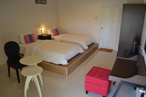 A bedroom with two beds, a small table, a chair, a red ottoman, and a TV. - Phudara Resort (Phu Ruea)