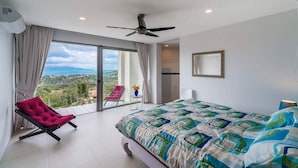 A bedroom with a bed, a chair, a ceiling fan, and a view of the outdoors.
