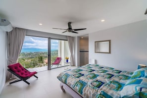 A bedroom with a bed, a chair, a ceiling fan, and a view of the outdoors.