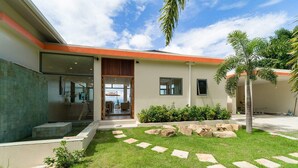 A modern house with a glass entrance, a stone pathway, and a well-maintained lawn.