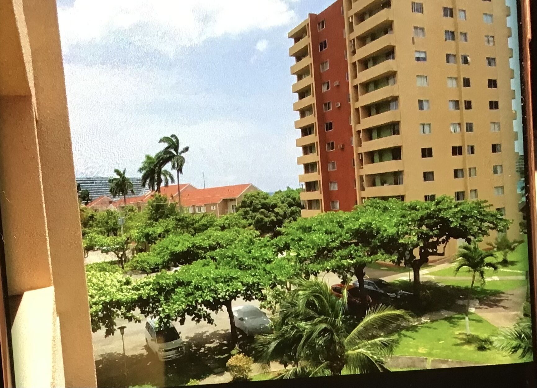 Une vue d’un quartier résidentiel avec un immeuble de grande hauteur, des arbres et des voitures garées.