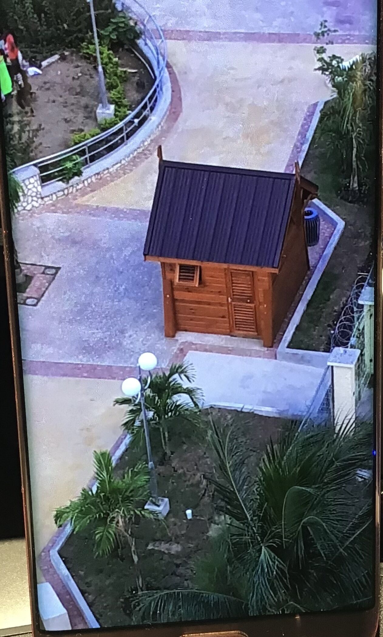 A small wooden cabin with a dark roof, surrounded by a paved area and some greenery.