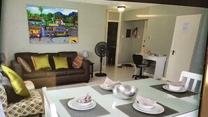 A dining area with a table set for four, a sofa with patterned cushions, and a painting on the wall depicting a tropical scene. - The McFarlane's Place is right in the heart of Ocho Rios Jamaica. (Ocho Rios)