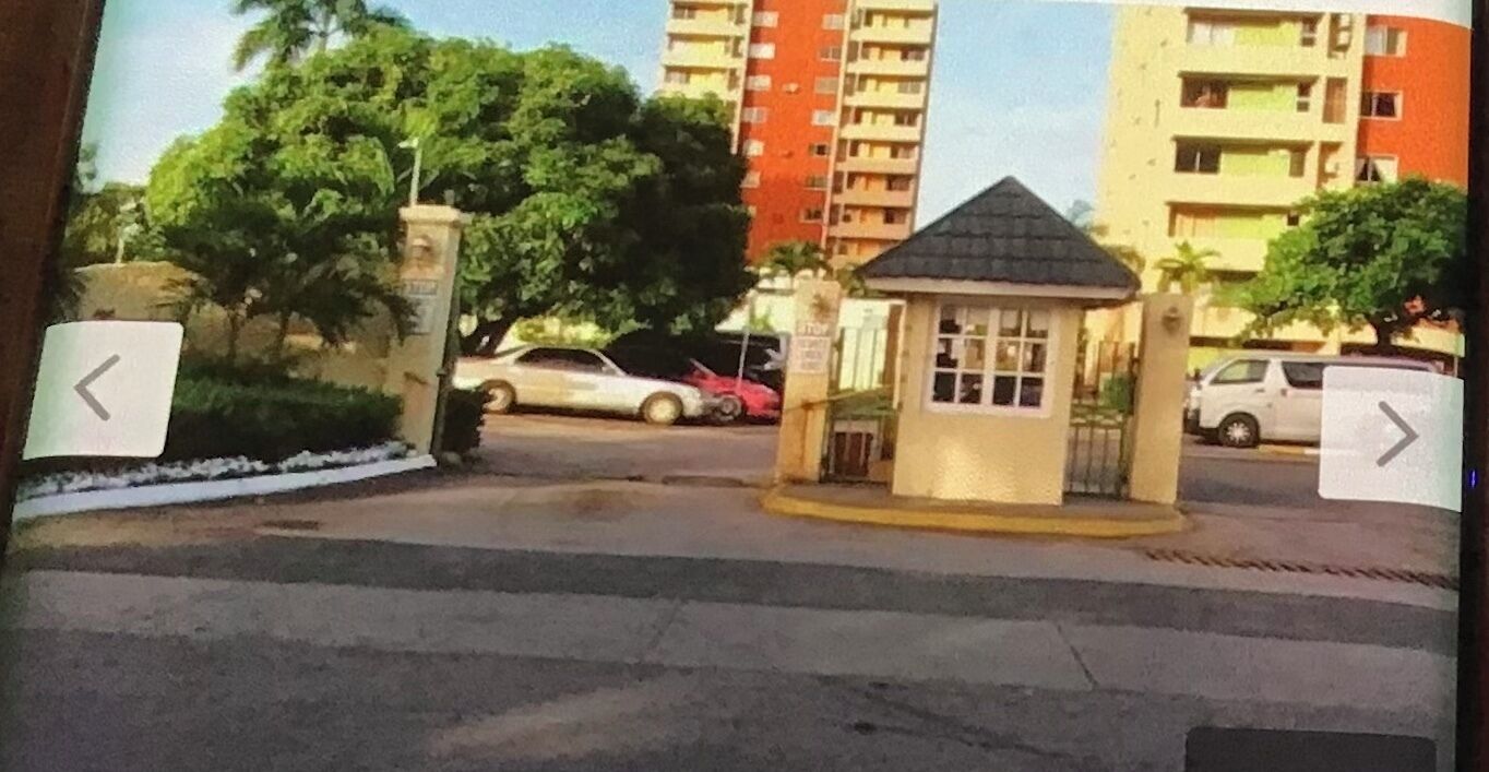Un quartier résidentiel fermé, doté d’un petit poste de garde, d’une route asphaltée et d’immeubles à plusieurs étages en arrière-plan.