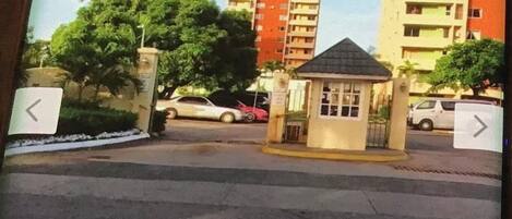 Un quartier résidentiel fermé, doté d’un petit poste de garde, d’une route asphaltée et d’immeubles à plusieurs étages en arrière-plan.