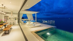 Un espacio habitable moderno y abierto con piscina, comedor y vista al océano al anochecer.