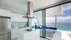 Una cocina moderna con una isla grande, horno empotrado y vistas al mar a través de puertas de vidrio amplias.