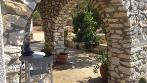 Un arco in pietra all'aperto con un tavolo e sedie, circondato da piante in vaso e un cactus.