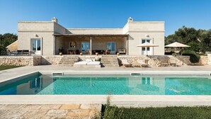 En moderne villa med swimmingpool, udendørs siddepladser og en facade af sten.