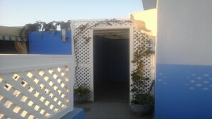 A narrow entrance to a building with a white lattice door, a blue wall, and potted plants on either side. - A Luminous and Spacious Medina House with a Rooftop Chillout Terrace  (Asilah)