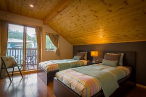 A bedroom with two beds, a wooden ceiling, a balcony with a chair, and a view of the outside. - Hakuba Powder Cottages (Hakuba)
