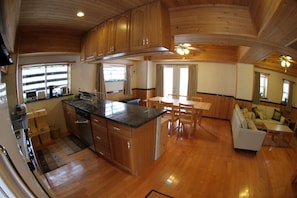 A spacious kitchen with wooden cabinets and a central island, a dining area with a table and chairs, and a living area with a sofa and a TV. - Hakuba Powder Cottages (Hakuba)