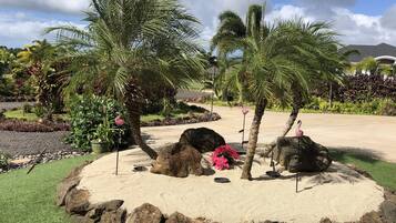 A landscaped garden with palm trees, rocks, and a flamingo statue.