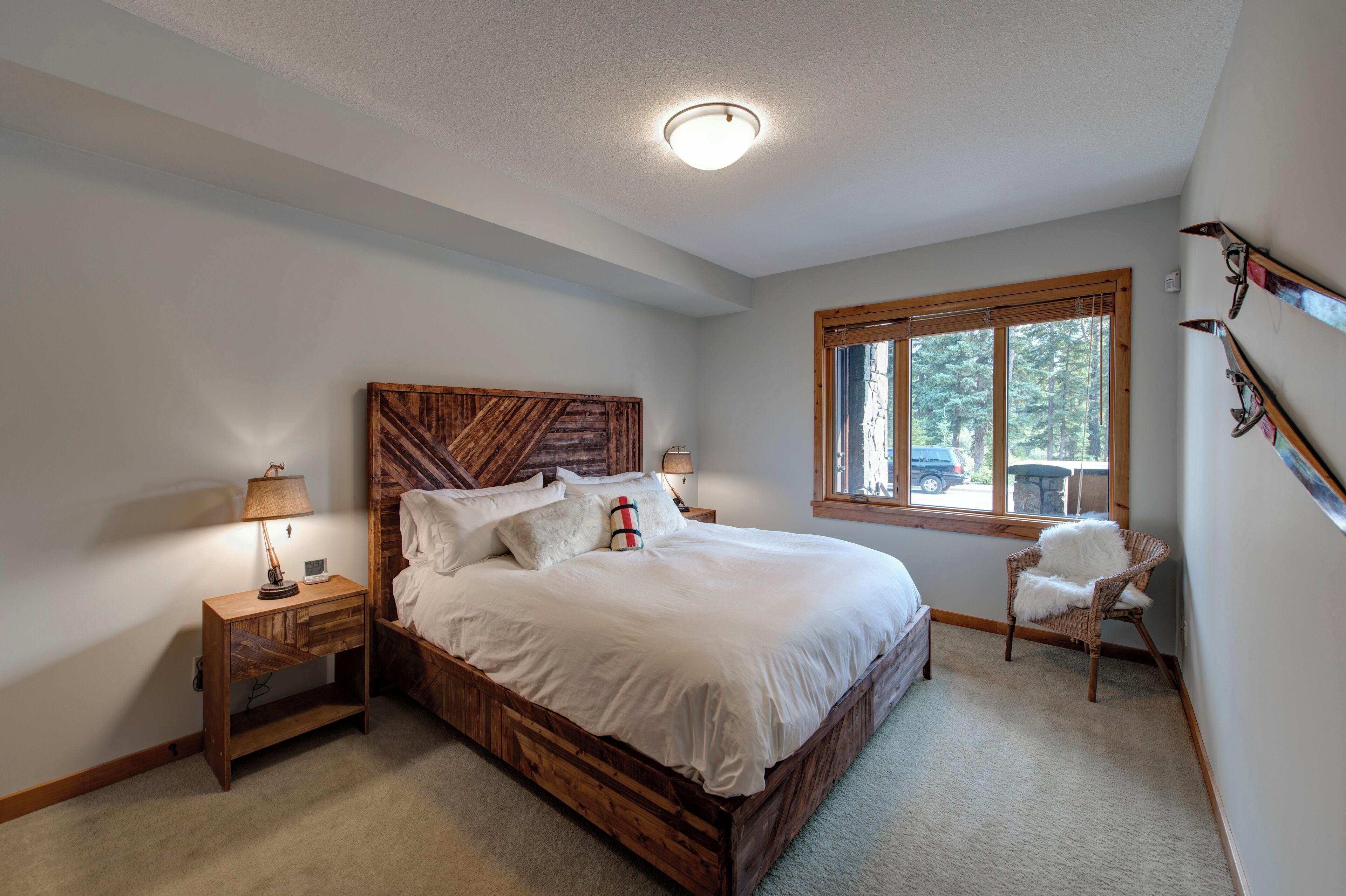 A bedroom with a wooden bed, a nightstand, a chair, and a window with a view of trees.