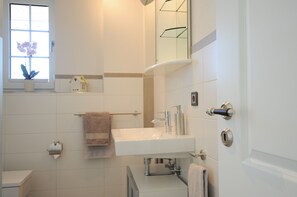 A bathroom with a white sink, a towel rack, a toilet, and a window with a potted plant.