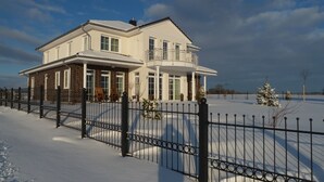 A two-story house with a balcony, surrounded by a snow-covered yard and a black metal fence.