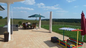 An outdoor patio with a table and chairs, a swing, and a play area with a striped board.