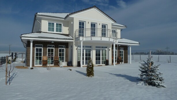 A two-story house with a large porch, multiple windows, and a snow-covered landscape.