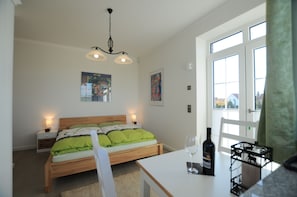 A bedroom with a bed, bedside tables, a table with a wine bottle and glass, and a window with a view.