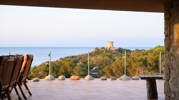 Eine Terrasse mit Stühlen und Tisch mit Blick auf eine Küstenlandschaft und ein Schloss.
