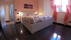 A bedroom with a bed, a nightstand, a wall-mounted lamp, and a window with curtains. - Arcobaleno Apartament  500 meters from the sea. (Albissola Marina)