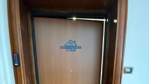 A wooden door with a logo, a doormat, and a light switch on the wall. - Arcobaleno Apartament  500 meters from the sea. (Albissola Marina)