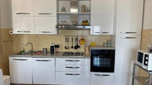 A kitchen with white cabinets, a gas stove, a microwave, and various kitchen utensils. - Arcobaleno Apartament  500 meters from the sea. (Albissola Marina)