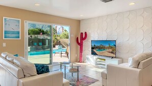 A modern living room with a pool view, white sofas, a glass coffee table, and a TV on the wall. - Fantastic Views and Reviews! Bright, Relaxing Oasis! (Palm Springs)