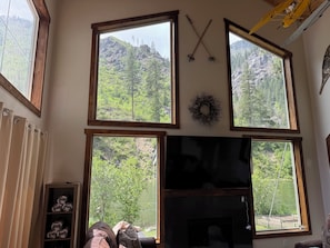 A room with large windows, a fireplace, and a wooden shelf with rolled-up items.