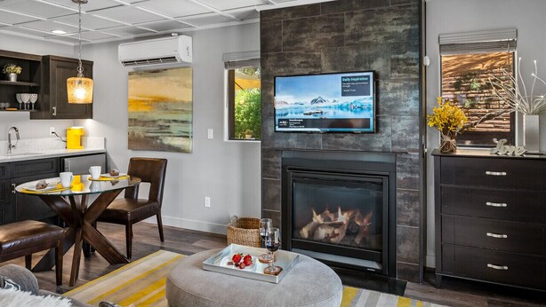 A modern living room with a fireplace, a dining area with a glass table, and a kitchen with dark cabinetry.