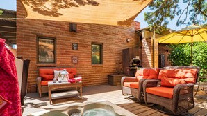 A cozy outdoor patio with wicker furniture, a hot tub, and a brick building.