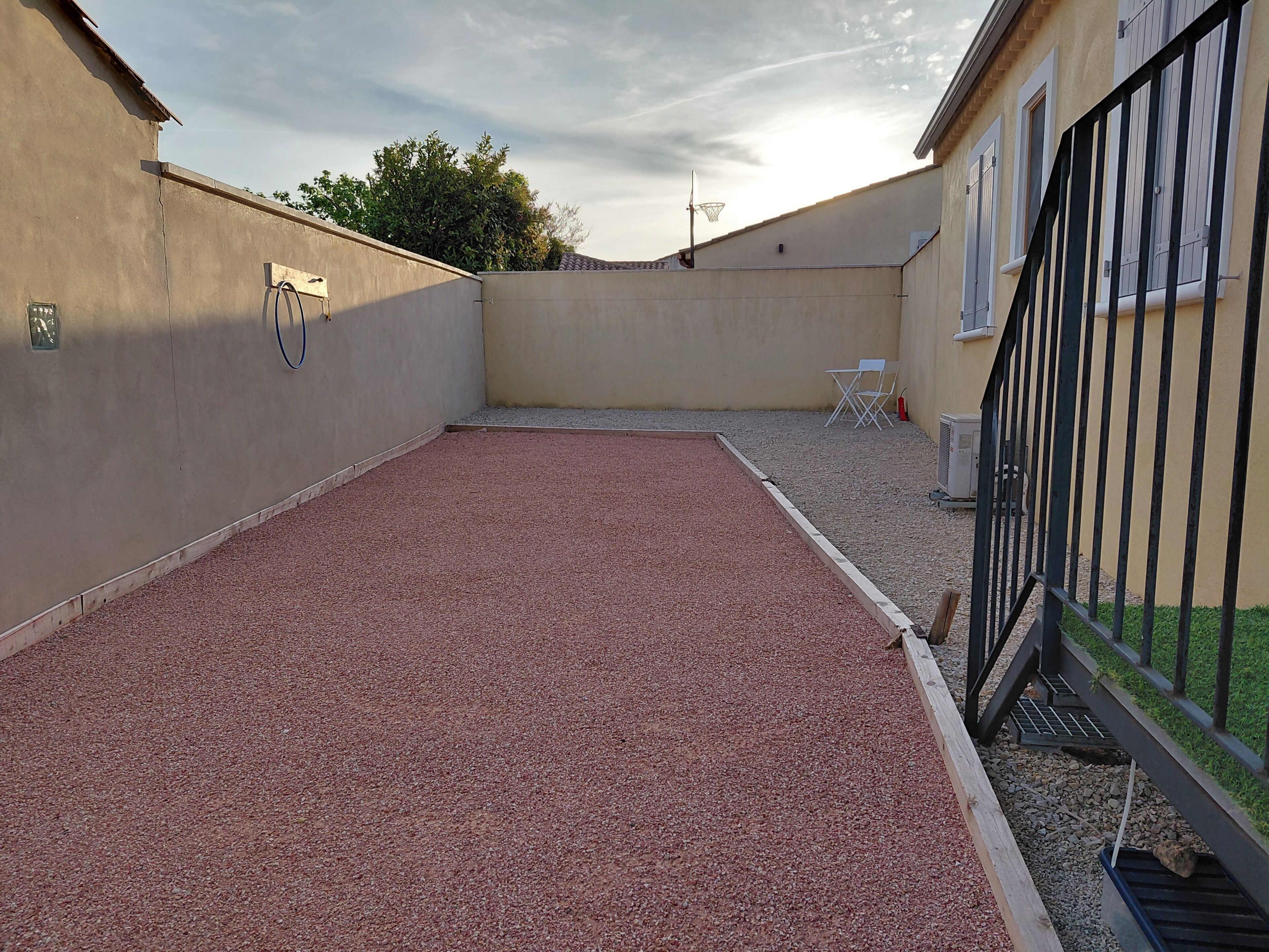 A rooftop with a red gravel surface, a basketball hoop, and a white folding chair.