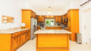 A kitchen with wooden cabinets, a large island, stainless steel appliances, and a view of the outdoors. - Costa A6 Beautiful Beachfront Property (Cozumel)