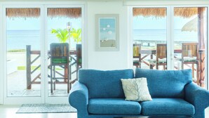A blue sofa with a cushion, a framed picture, and a view of the ocean through glass doors. - Costa A6 Beautiful Beachfront Property (Cozumel)
